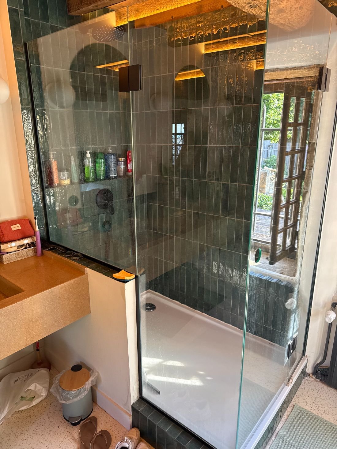 Douche à paroi vitrée et carrelage vert après rénovation, paroi et receveur couverts de poussière