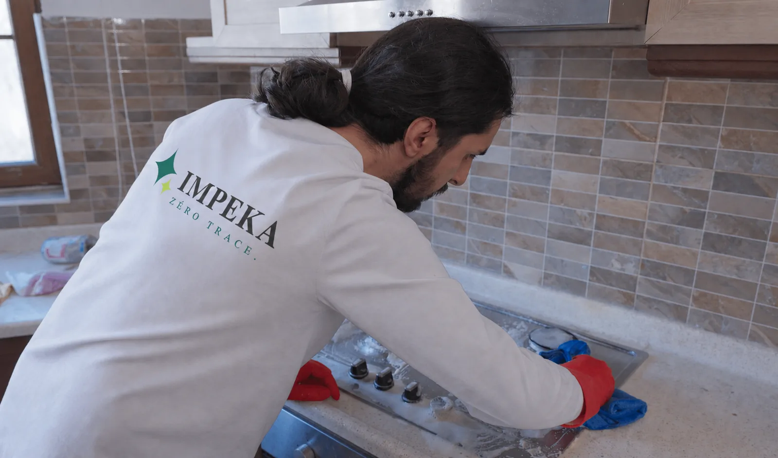 Agent IMPEKA en polo dégraisse une plaque de cuisson lors d'un nettoyage d'appartement à Paris